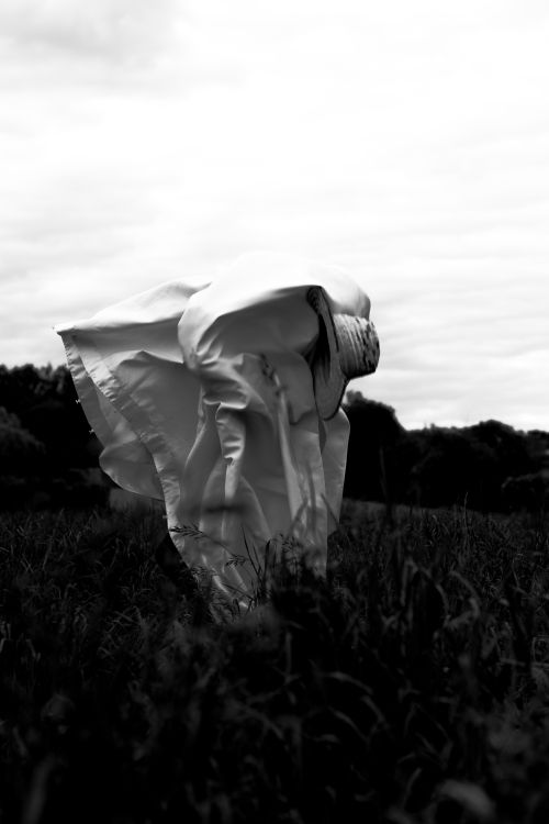 Free A mysterious figure in white cloth stands in a field under a cloudy sky. Stock Photo