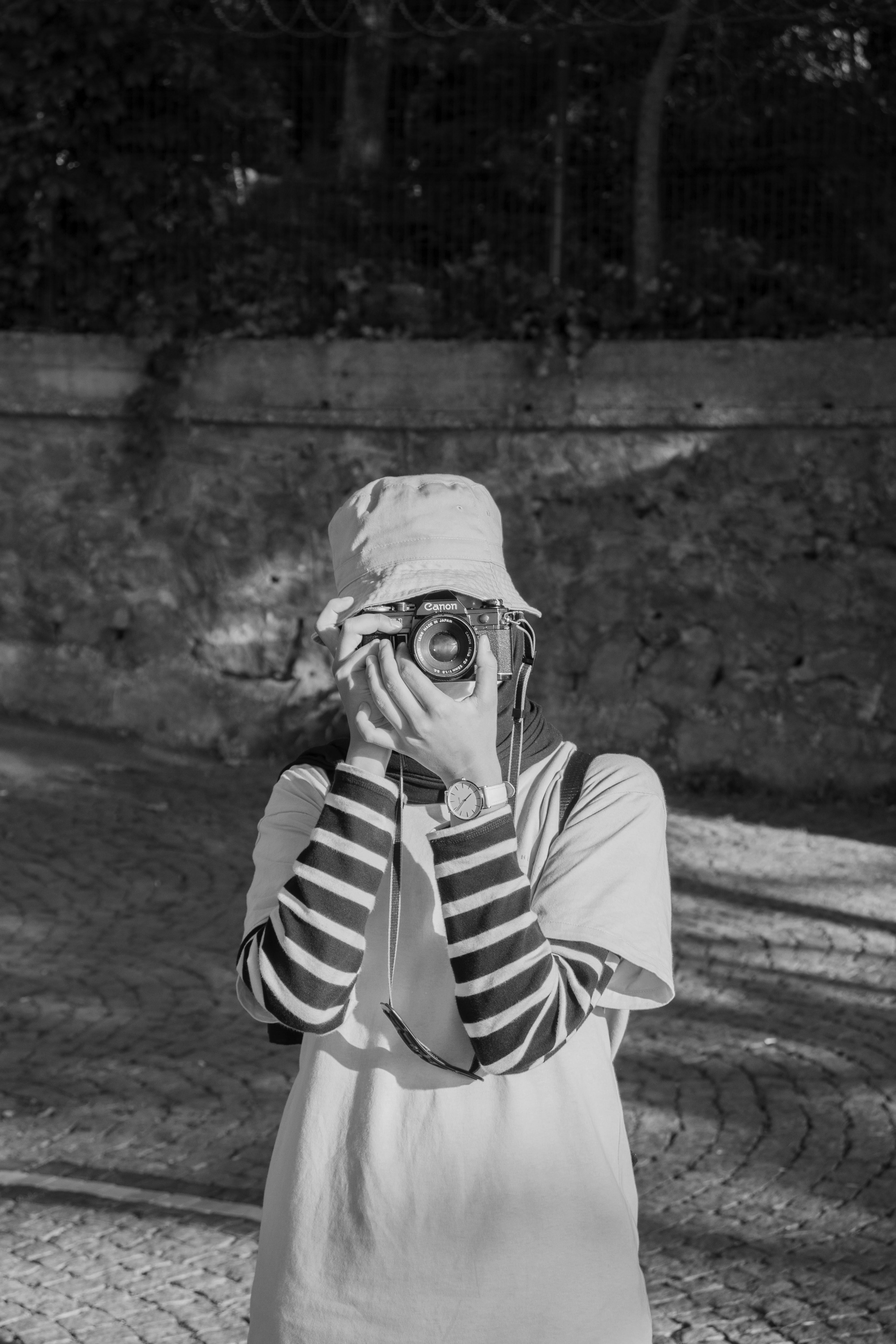 Black and white photo of a woman taking a picture outdoors in casual attire.