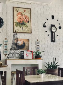 A beautifully decorated cafe with vintage elements, wall art, and a classic clock on a white brick wall.