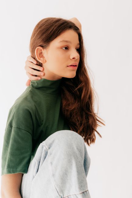 Studio portrait of a young girl with long brown hair, wearing a green turtleneck, thoughtful pose.