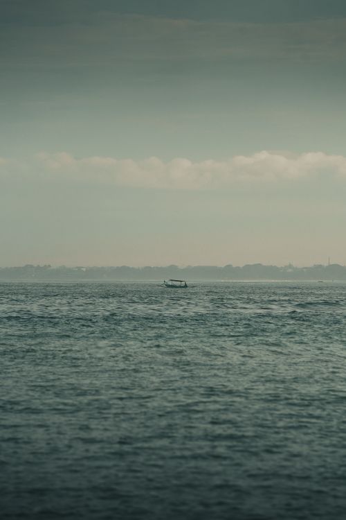 Free Calm ocean view with a solitary boat against the Bali skyline, evoking tranquility. Stock Photo