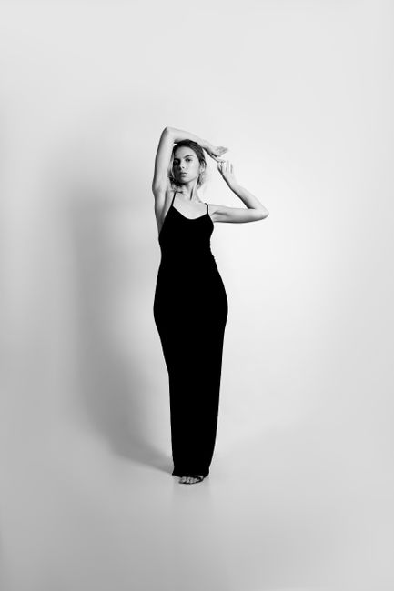 Black and white portrait of a woman posing elegantly in a long black dress with arms raised.
