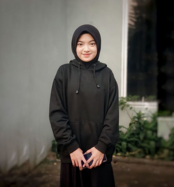 Portrait of a young woman wearing a black hijab and hoodie standing outdoors.