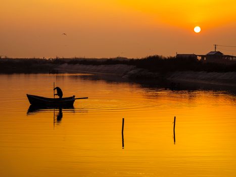 A serene scene of a fisherman in a canoe silhouetted against a vibrant sunset over calm waters.