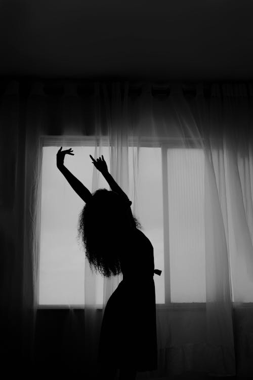 Silhouette of a Woman Dancing against Window with White Curtain