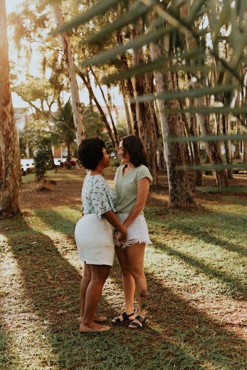 Women in White Shorts Standing in a Park and Holding Hands