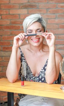 Smiling woman in a floral dress holding lipstick indoors, São Paulo setting.