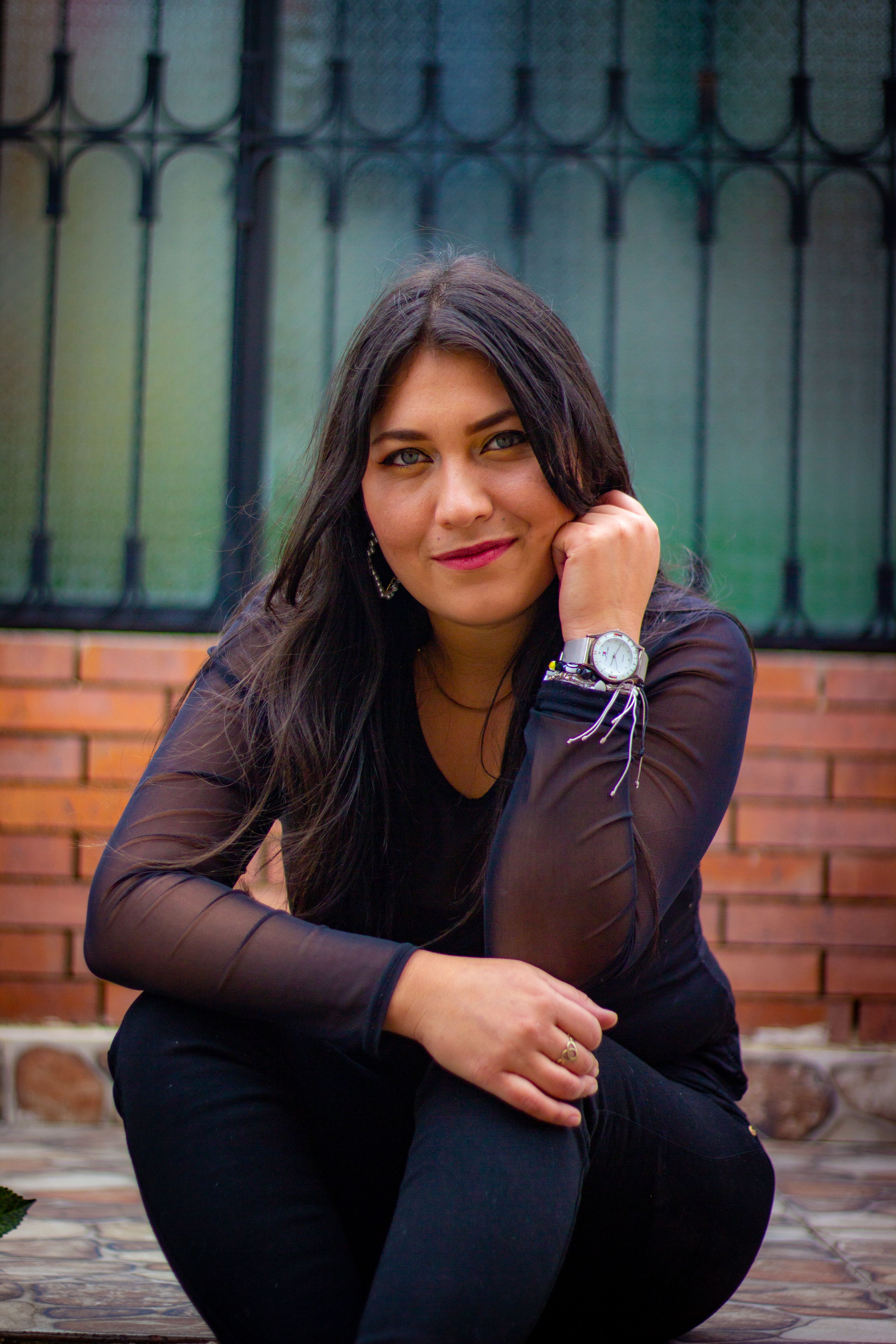 Portrait of a young woman sitting on a curb, wearing a wristwatch, outdoors.