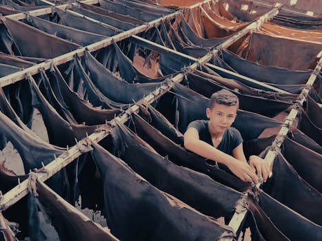 A young boy works in a traditional leather tannery, surrounded by hanging hides.