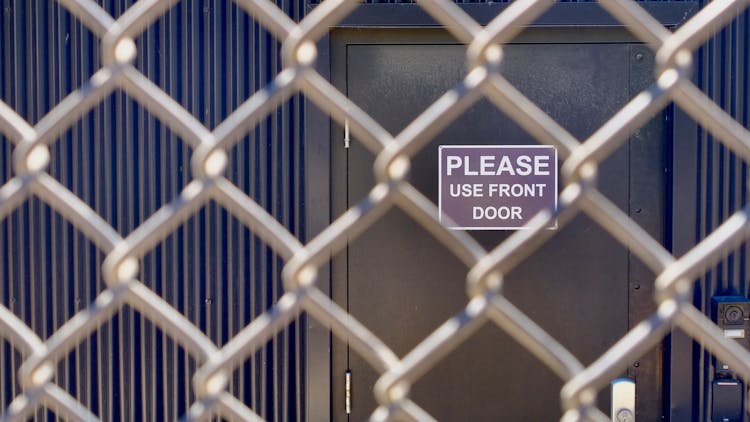 The Backdoor Entrance Of A Building Beyond A Wire Mesh Fence