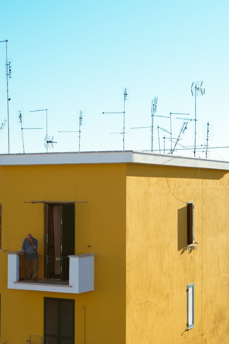 Man Standing On Balcony Of A Yellow Concrete Building