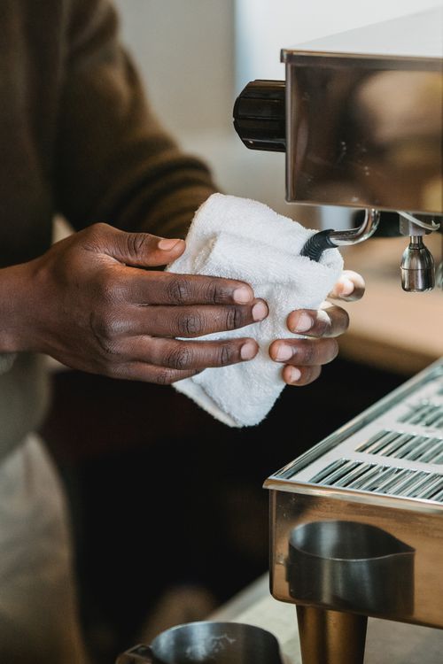 Free Close-up of a barista cleaning an espresso machine with a cloth inside a coffee shop. Stock Photo
