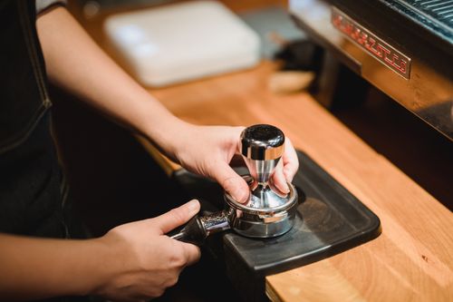 Free Close-up of barista hands tamping espresso grounds using a portafilter in a cozy café setting. Stock Photo
