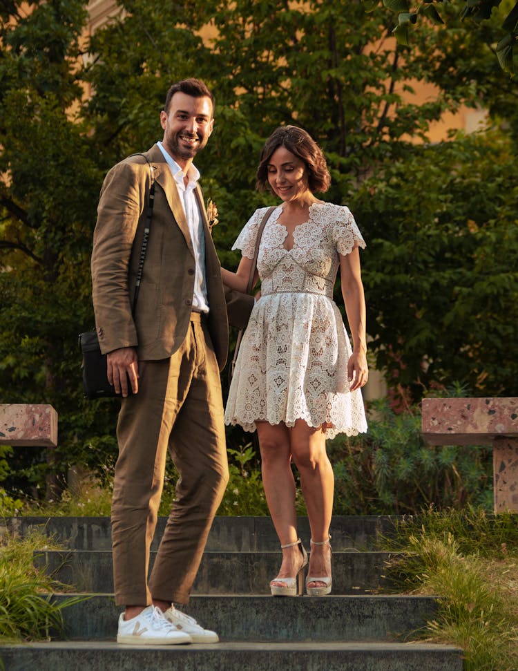 Man Wearing A Brown Suit Standing In A Park With A Woman Wearing A Lace Dress