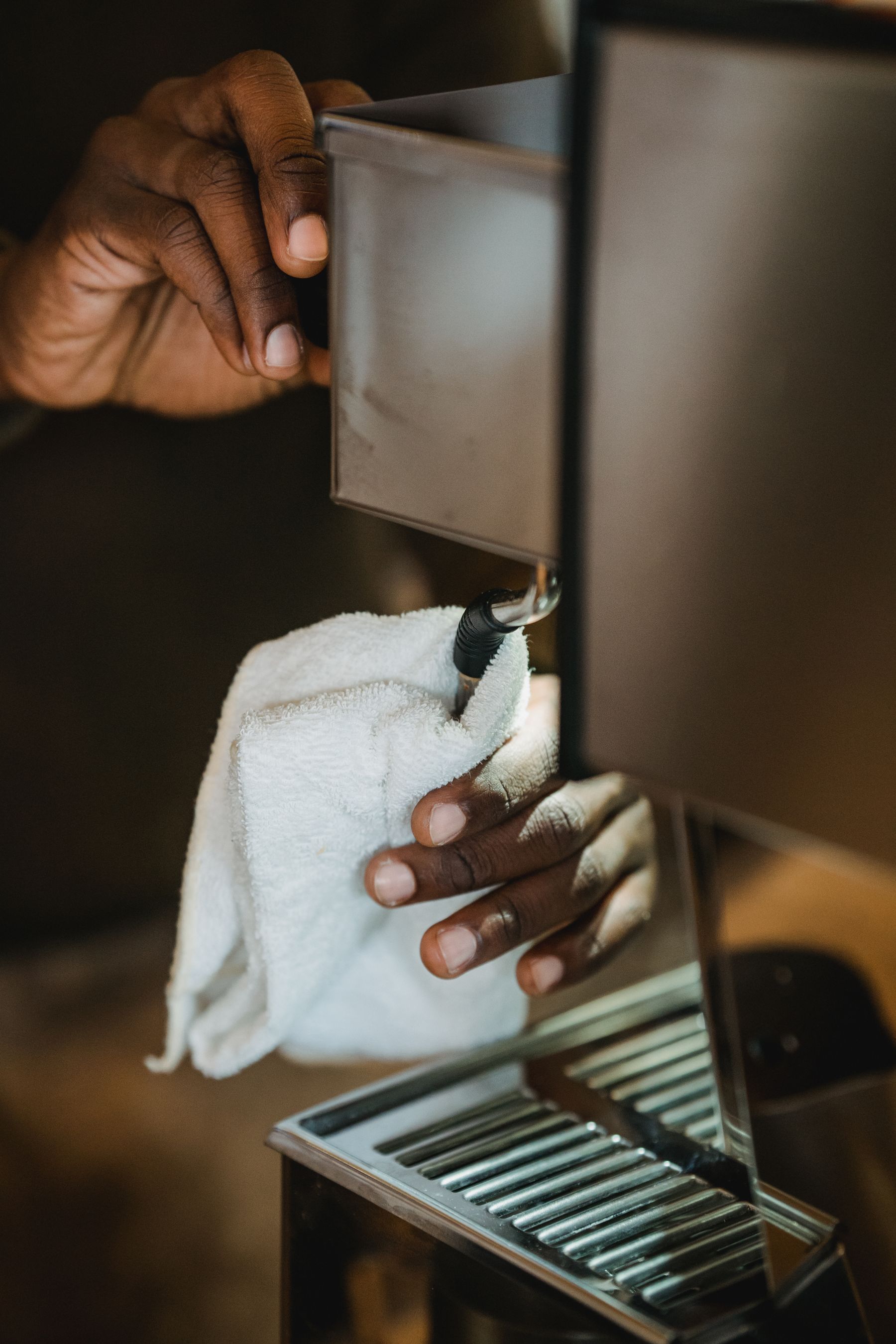 Hands carefully wiping the metal surfaces of a coffee machine during a routine cleaning session