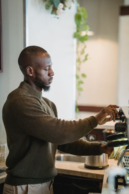 Free Black male barista making fresh coffee in a warm café setting, showcasing coffee culture. Stock Photo