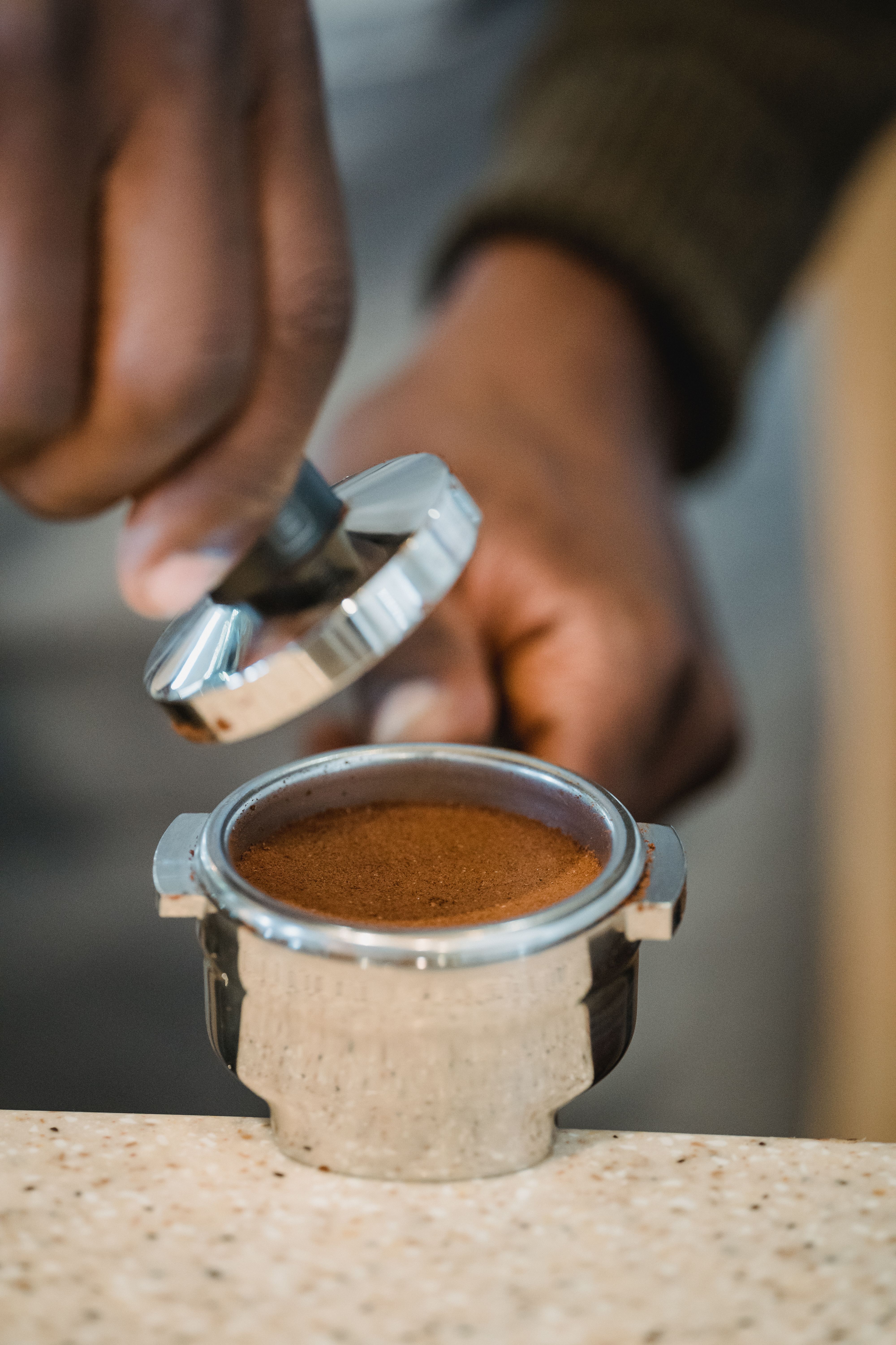 Barista's hands tamping fresh coffee grounds into a portafilter