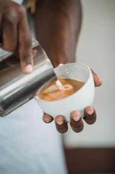 Close-up of barista pouring latte art into a cup in a cozy café setting.