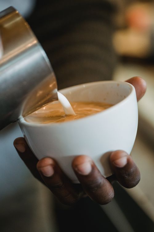 Free Barista expertly pours milk into a steaming cappuccino, showcasing coffee art. Stock Photo