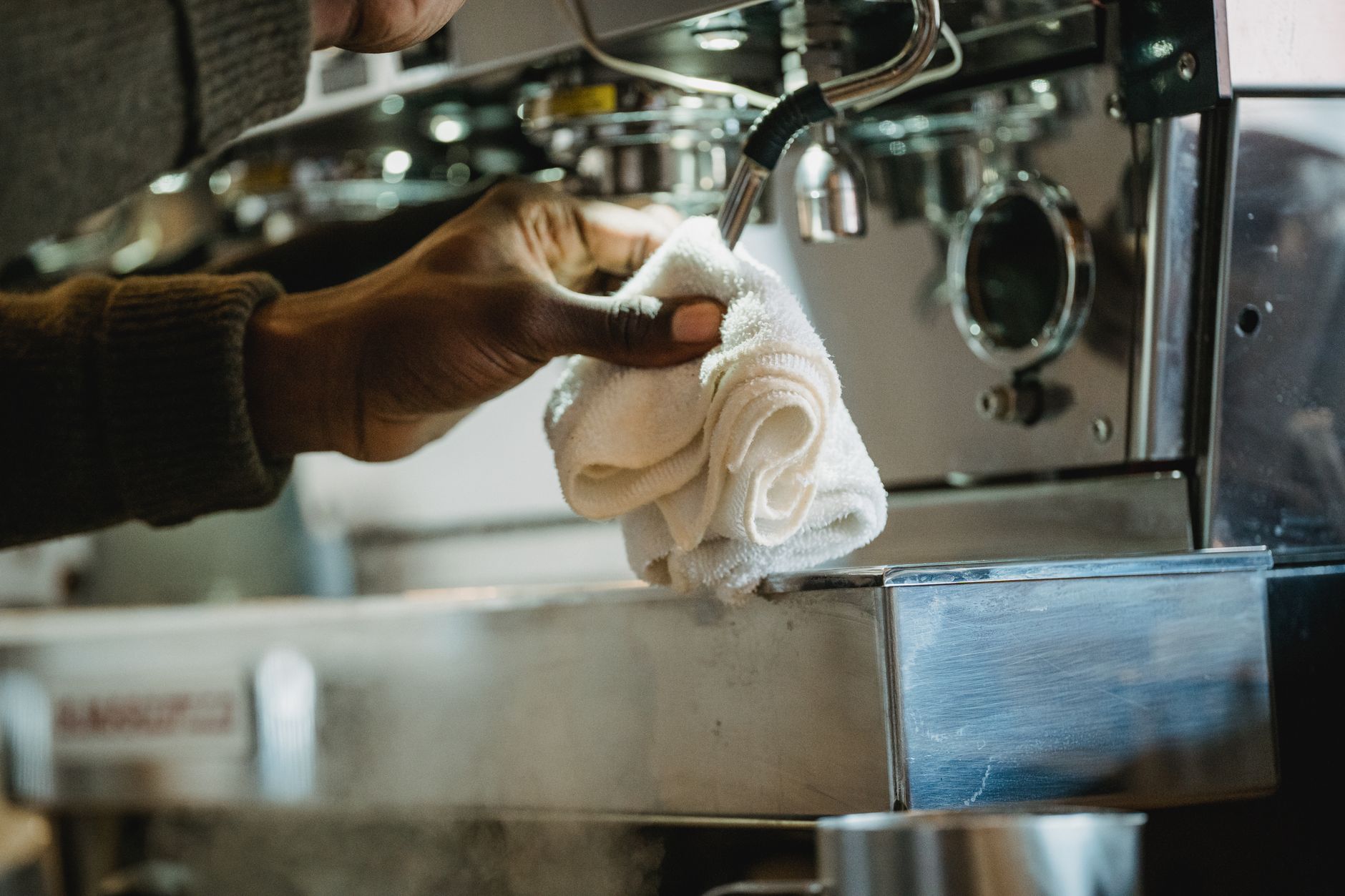 Close-up of a person cleaning a coffee machine using a cloth. Focus on hygiene and maintenance.