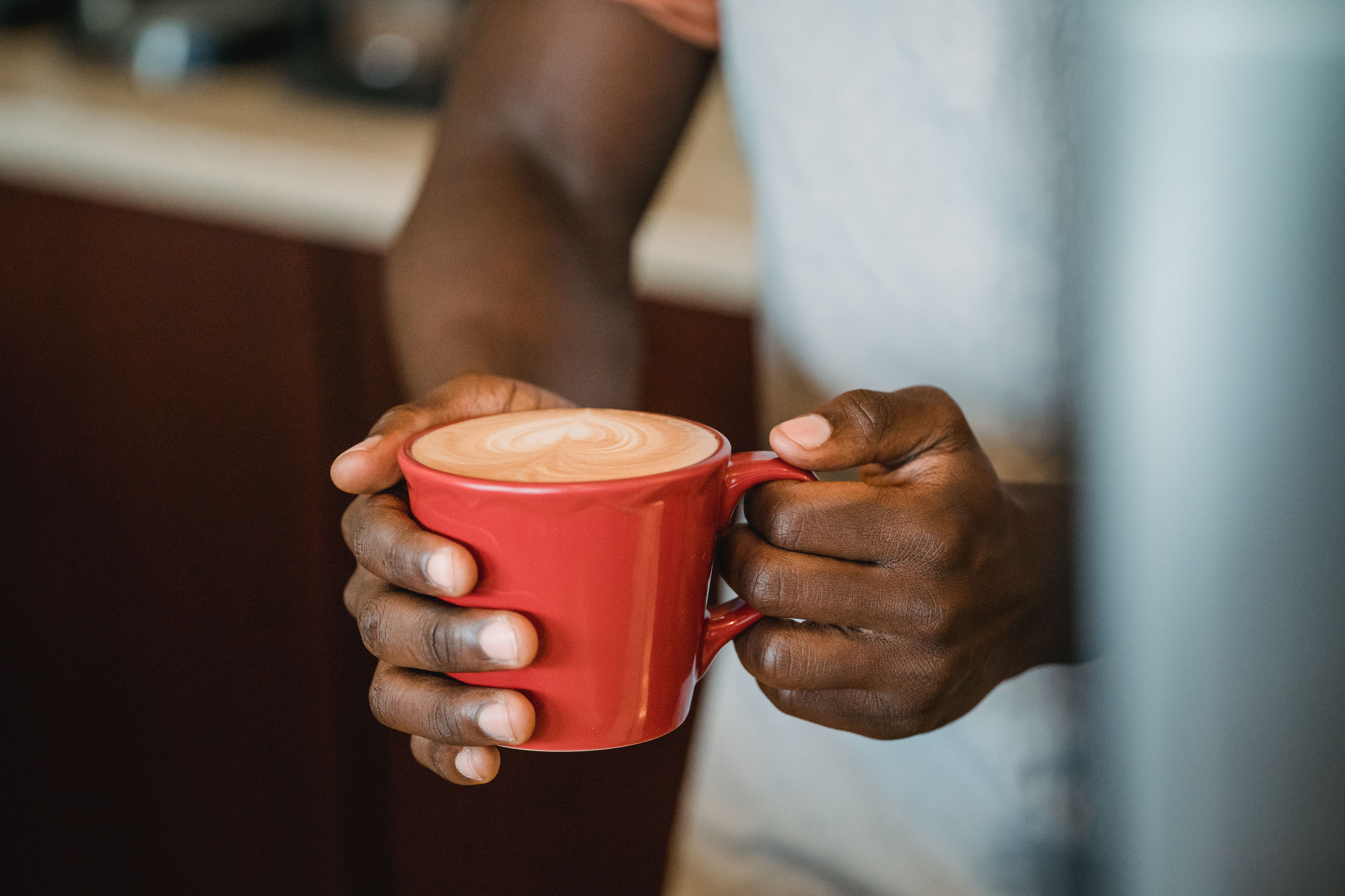 Person holding a red cup of coffee with intricate latte art in a cozy café setting.. person, holding, coffee