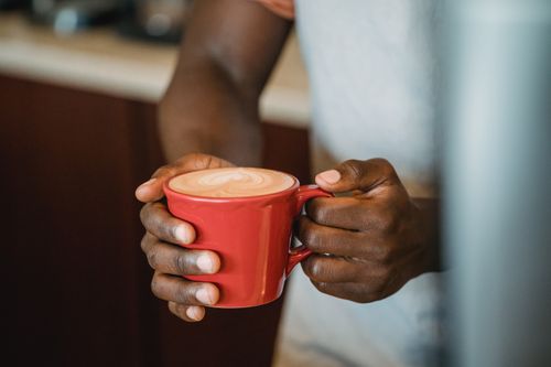 Free Person holding a red cup of coffee with intricate latte art in a cozy café setting. Stock Photo