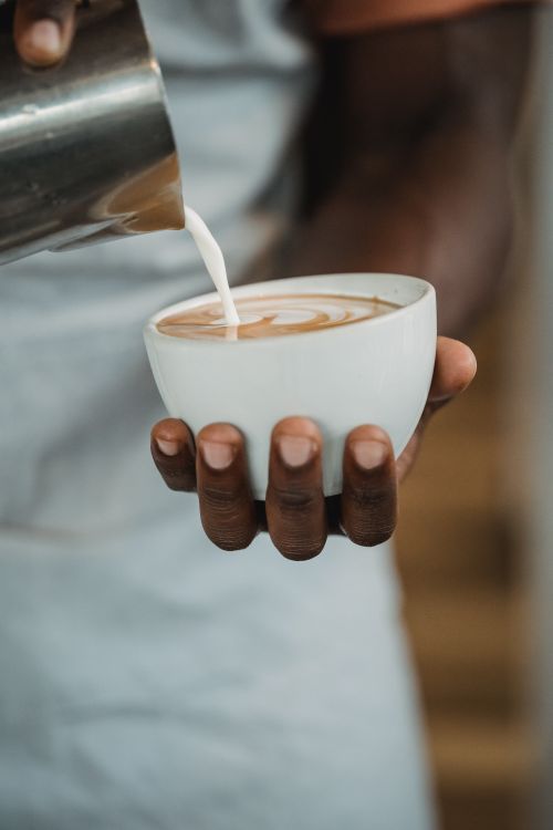 Free Close-up of barista crafting latte art with milk in a café setting. Stock Photo