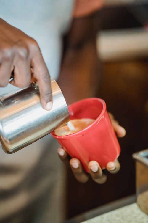 Free A barista skillfully pouring frothy milk into a cup for a delicious latte, captured in a cozy café. Stock Photo