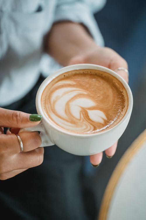 Free Close-up of a woman's hands holding a cup with beautiful latte art in a café setting. Stock Photo