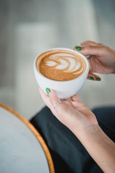 A serene moment as a woman holds a latte with intricate art, perfect for relaxing.