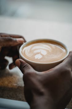A close-up shot of hands holding a cup of latte with beautiful latte art design.