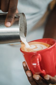 Close-up of a barista pouring milk into a coffee cup, creating latte art. Perfect for coffee enthusiasts.