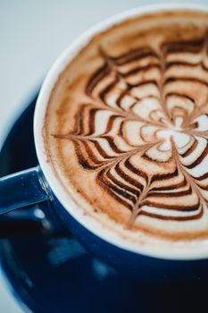 Close-up of a beautiful latte with artistic cocoa powder design in a blue cup.