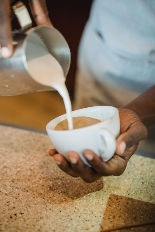 Free Close-up of barista's hands pouring milk into coffee mug in a café setting. Stock Photo