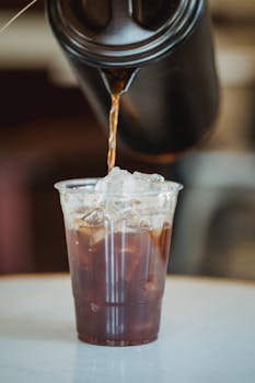 Close-up of iced coffee being poured into a plastic cup in a café. Perfect for beverage themes.