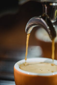 Close-up of espresso pouring into an orange cup from a coffee machine. Perfect for coffee enthusiasts.