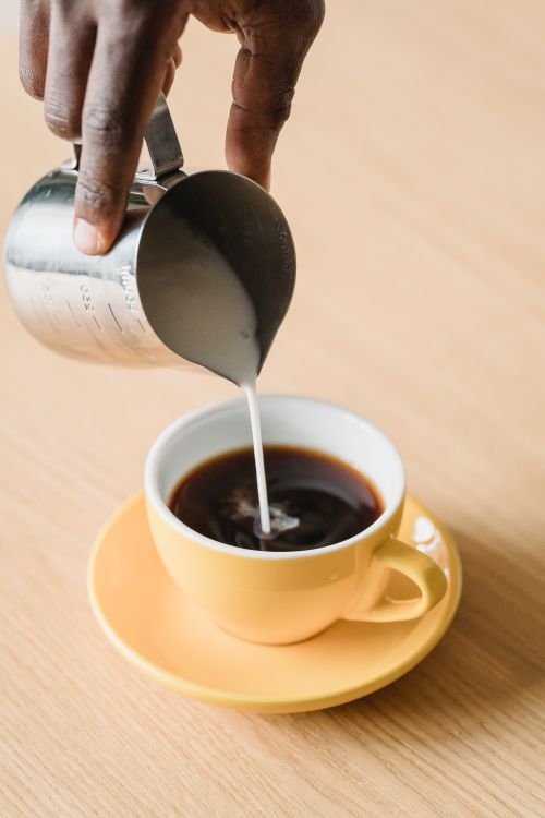 Free A close-up view of milk being poured into a coffee cup, showcasing a hand holding a pitcher. Stock Photo