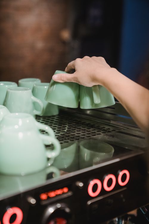 Free Close-up of a hand arranging mint green cups on a coffee machine in a café. Stock Photo