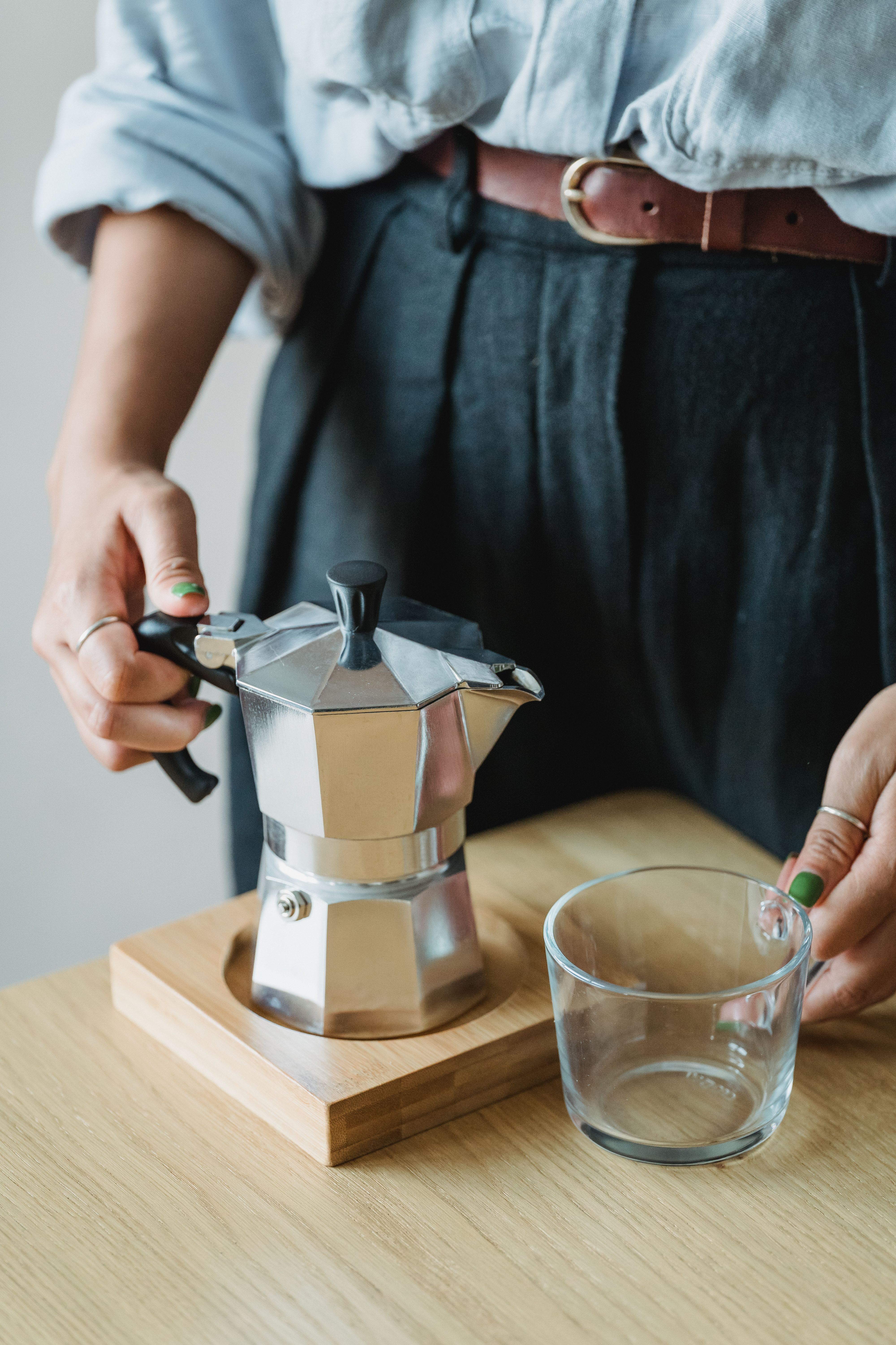 Close-up of a woman holding a moka pot near a glass cup on a wooden table.