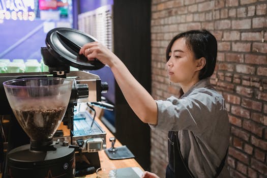 A focused barista prepares coffee using a grinder in a cozy, brick-walled café setting.