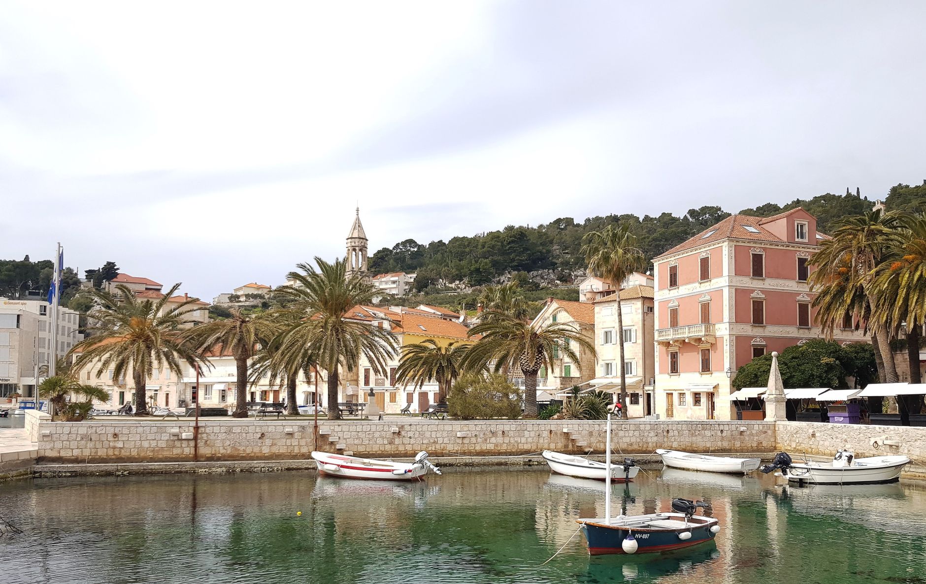 Boats moored in Hvar Town harbour beside palm trees and stone buildings, a stop on the Split to Dubrovnik ferry route