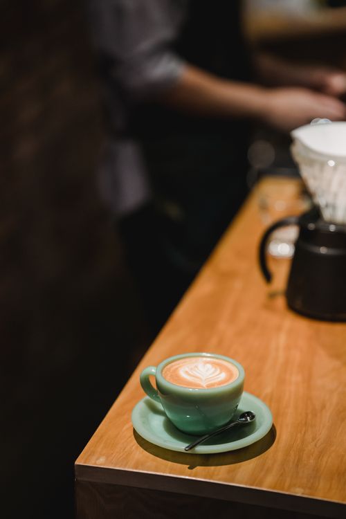 Free A close-up of a beautifully decorated latte on a wooden café table, creating a warm and inviting atmosphere. Stock Photo