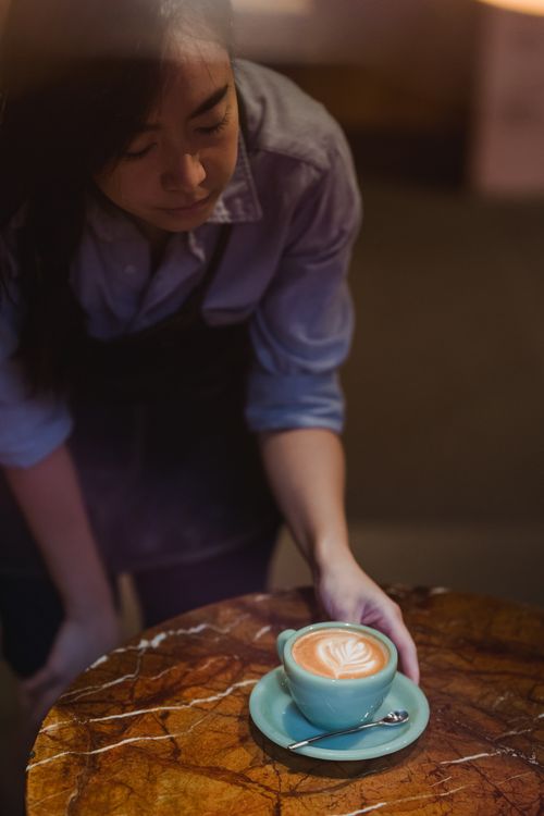 Free A barista places a cup of latte with intricate foam art on a marble table. Stock Photo