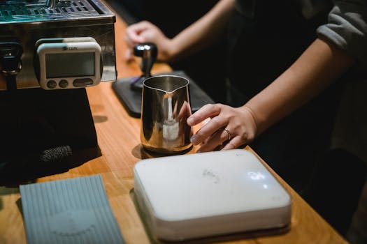 A barista preparing coffee with a milk frother and tamper in a café setting.