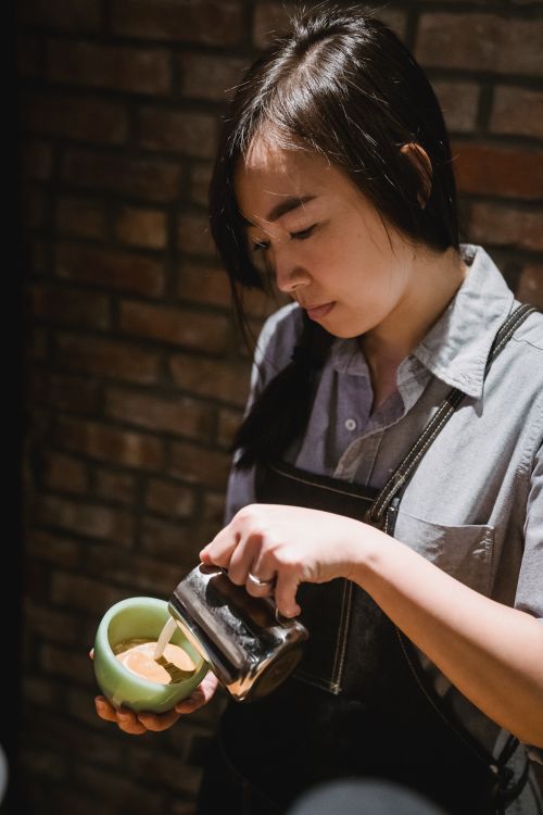 Free Barista focused on pouring milk into a coffee cup, showcasing her precision and artistry. Stock Photo