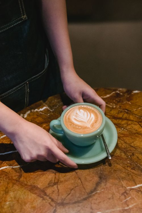 Free A barista presents a cup of cappuccino with latte art on a marble table, showcasing coffee culture. Stock Photo