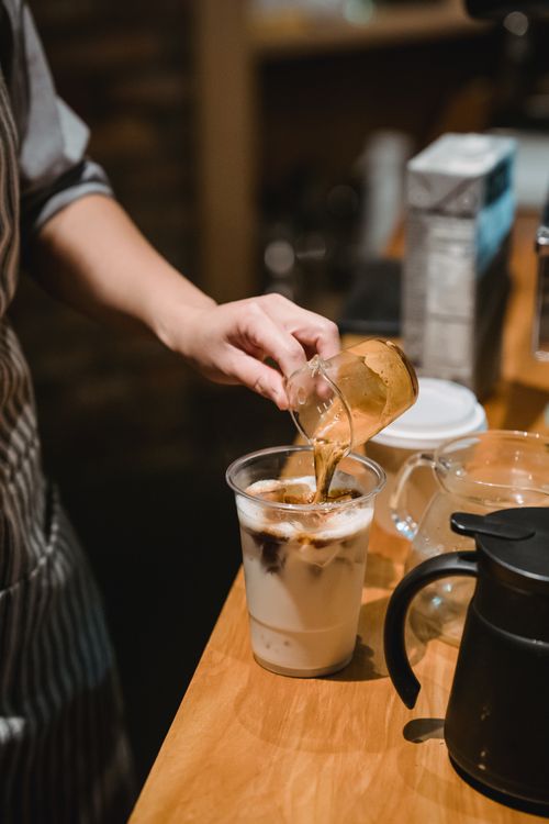 Free A barista skillfully pours espresso into iced coffee at a cozy café. Stock Photo