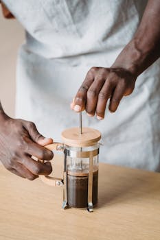 Barista pressing coffee in a French press on a wooden table.