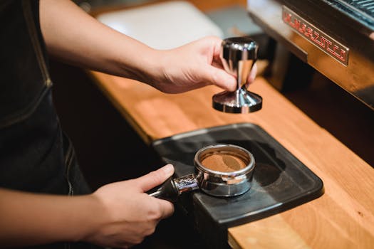 Close-up of a barista pressing coffee grounds using a tamper at a café.