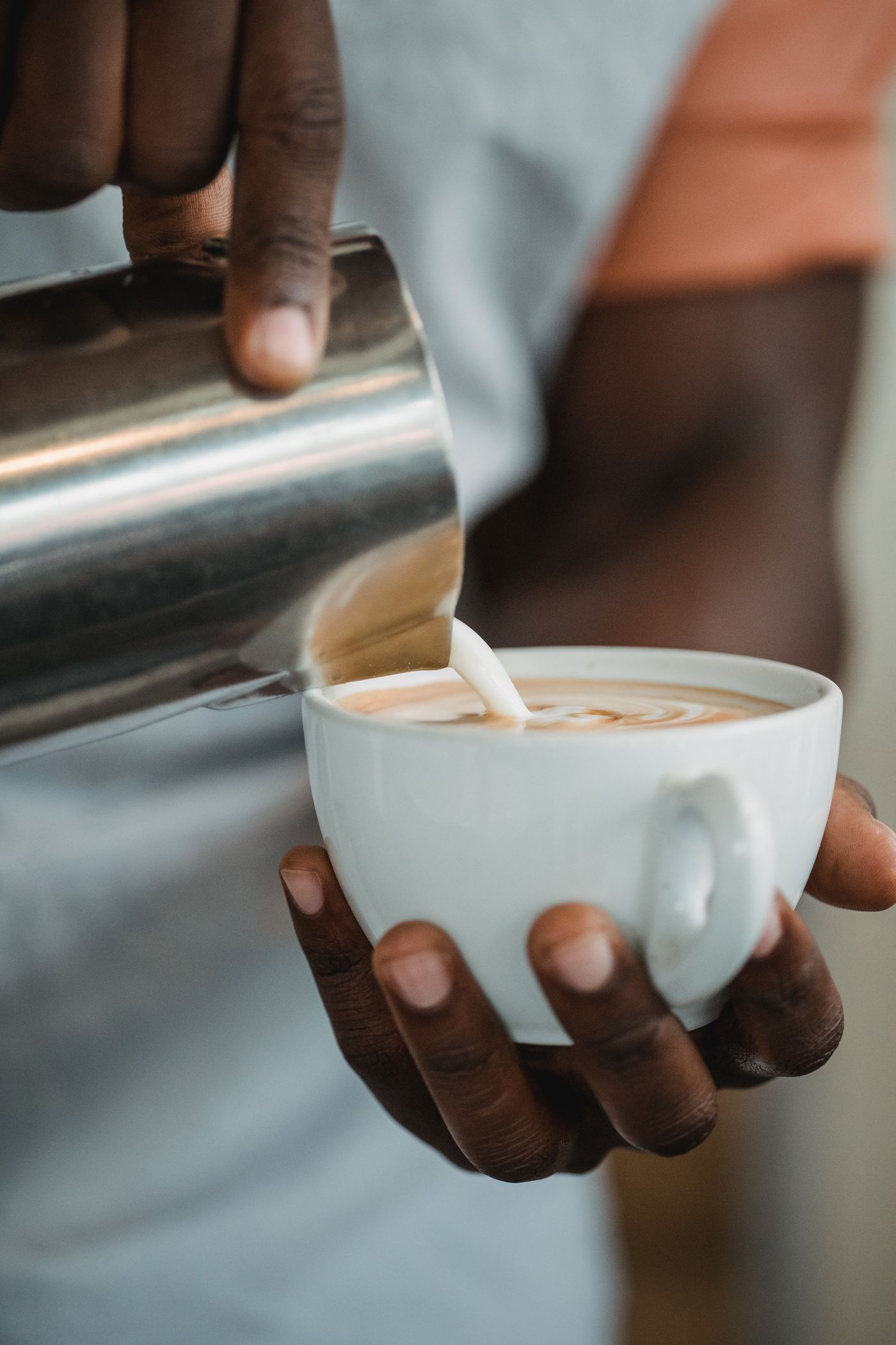 Unbranded stainless-steel milk pitcher pouring latte art into a cappuccino